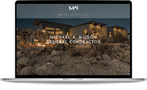 lapmock-michaelwilson A laptop displaying a website for Michael A. Wilson, General Contractor, featuring a modern house in a rocky, desert landscape. The website has navigation links for Home, About, Portfolio, and Contact.