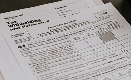A close-up of IRS tax forms, including Schedule D and Publication 505, showing sections for capital gains and losses and estimated tax calculations.